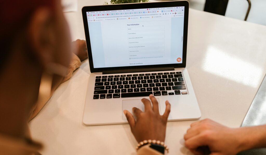 Two adults working together on a laptop displaying an online form, indoors.